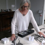 Woman with black framed glasses touching drawings of insects on a table.